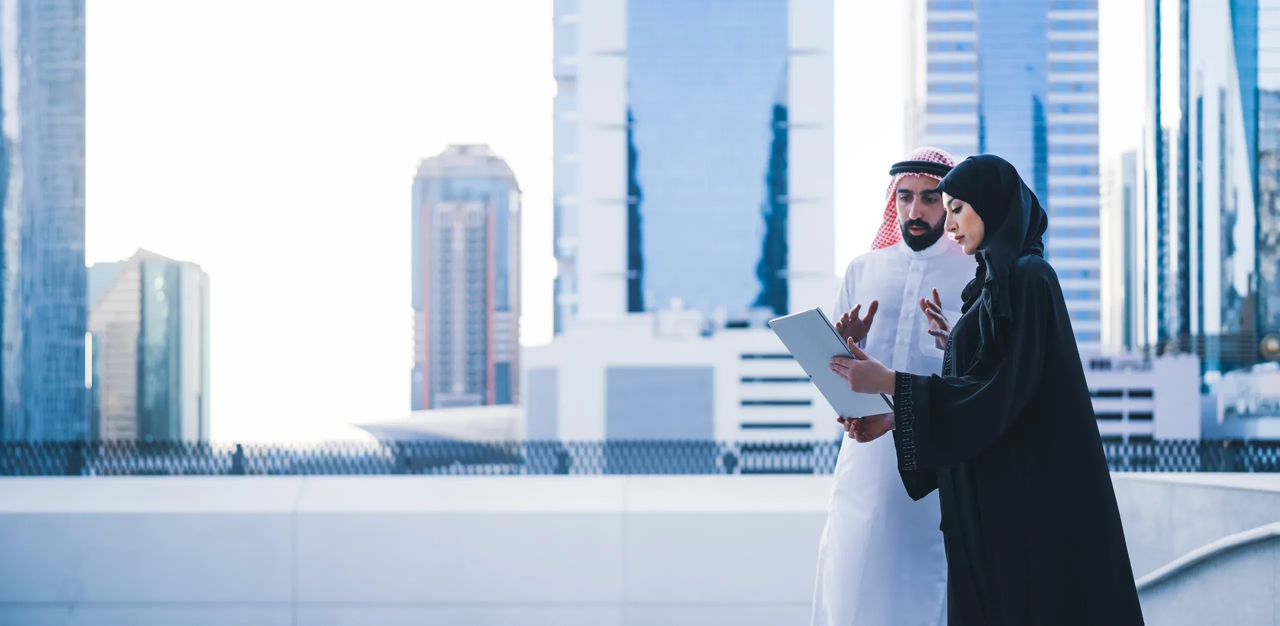 Two business people in Arabic dress stand in front of commercial buildings. 